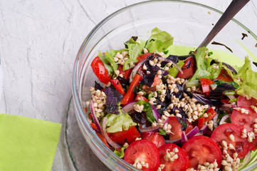 vegetarian fresh salad with vegetables, herbs and  sprouts  of buckwheat.  beautiful served in transporant bowl at white table. healthy raw eating food. close up