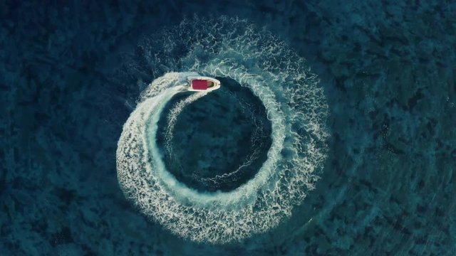 Slow motion aerial shot descending towards fast speedboat with a red roof top, going around in the circle and making beautiful shapes in the clear sea. Top travel destination. 4K.