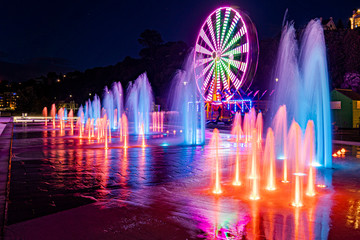 A display of colored fountains and ferris wheel at night