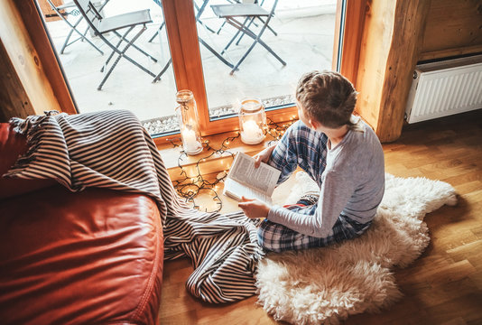 Boy reading book on the floor on sheepskin in cozy home atmosphere. Peaceful moments of cozy home concept image.