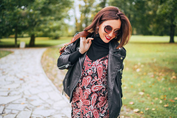 Smiling female dressed boho fashion style colorful long dress with black leather biker jacket with...