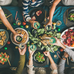 Company of friends gathering for Christmas or New Year party dinner at festive table. Flat-lay of hands holding glasses with drinks, feasting and celebrating holiday together, top view, square crop