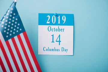 paper calendar with Columbus Day inscription near American national flag on blue background