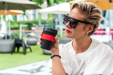 Businesswoman sitting in the garden during day holding reusable coffee cup