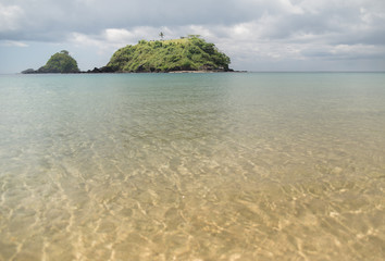 Small desert island with a shallow sandy lagoon in the foreground among stormy skies filled with rain clouds in a tropical paradise during monsoon season