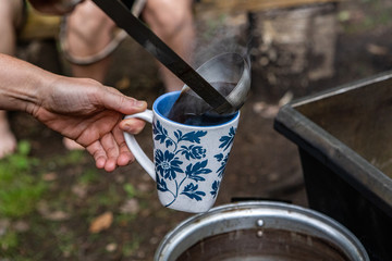 Fototapeta na wymiar Diverse people enjoy spiritual gathering A close up view of a person using a ladle to serve steaming hot tea from a camp fire stove during a retreat dedicated to healthy body and mind.