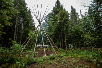 Diverse people enjoy spiritual gathering A tipi (teepee) tent skeleton is seen erected in a forest clearing on a sacred site where people gather to experience native tribal cultures. © Valmedia