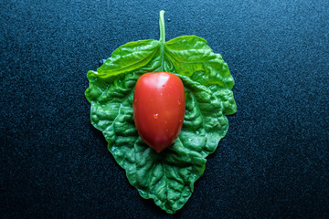 Plum tomatoe on big basil leaf. Top view. Black background. copy space