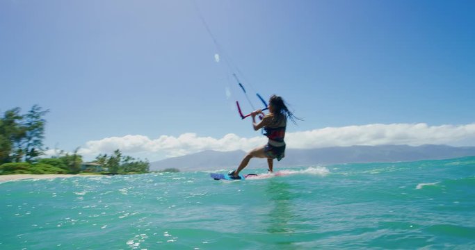 Young active woman kitesurfing and jumping into the air doing a 360 aerial maneuver, extreme sports in paradise