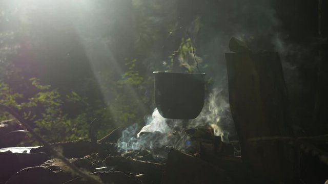 Cooking in a pot over campfire in forest. Campfire outdoors in national park. Cooking meal with open fire and old coocking equipment. Campfire with intence flame and smoke.