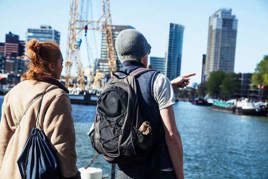 Young Couple Tourists Looking And Pointing To Rotterdam City Harbour, Future Architecture Concept, Industrial Lifestyle People