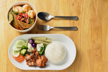 yellow curry with acacia vegetable omelette served with deep fried chicken wing sticks, rice and variety of fresh vegetable on wooden table