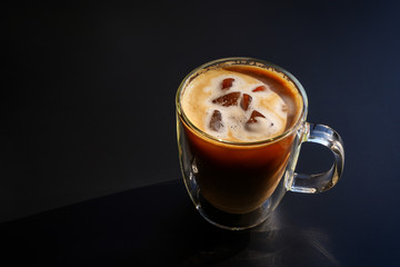 Top view, iced coffee with milk foam on top, double-layer glass on a black background.