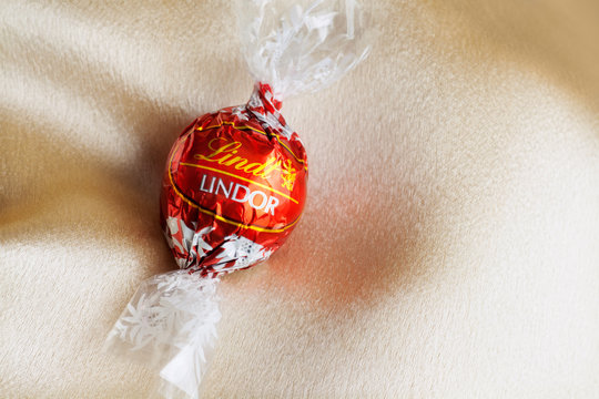 Lindt Chocolate bon bon by Lindor in red foil wrapper on silky smooth satin background with room for copy space
