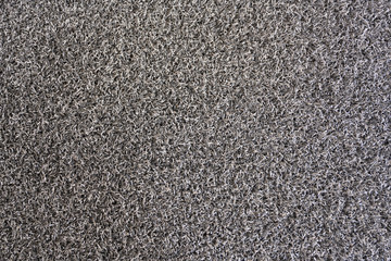 The floor mat is made of plastic PVC mixed with synthetic rubber. Soft, sponge-like texture with a dark gray color.