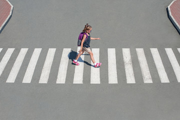Schoolgirl crossing road on way to school. Zebra traffic walk way in the city. Concept pedestrians passing a crosswalk. Stylish young teen girl walking with backpack.  Active child. Top view