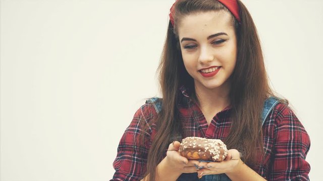 Lovely young female proposing you to taste big chocolate doughnut, showing by her face expression that it is very tasty.