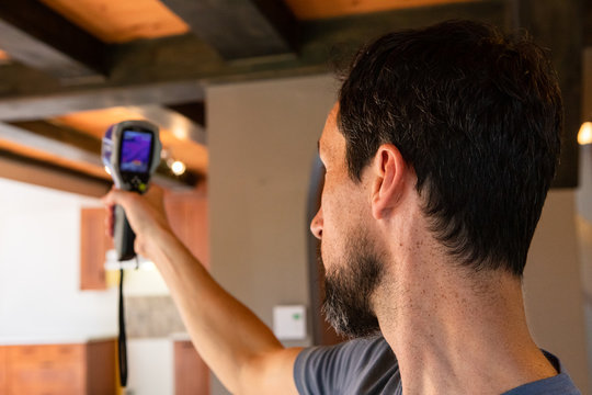 Indoor damp & air quality (IAQ) testing. A close up and side view on the head of a building surveyor carrying out an in-depth assessment of a domestic house, using a thermal spot imaging camera.
