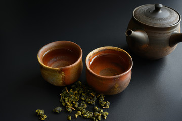 Teapots and two cups and tea leaves on a black background shot on the top view.