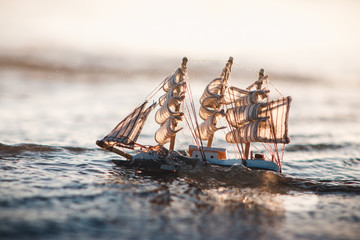 Toy boat sailing in the sea with sunset background