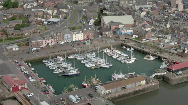 An aerial view of Arbroath harbour and town on a cloudy day. Tracking forward and down towards the harbour entrance with the town in the background with zoom in.