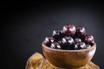 A wooden cumbuca with many jabuticabas, is a Brazilian pulp fruit with low calories and carbohydrates, and has large amounts of vitamin C. Exotic and healthy fruit, natural life concept.