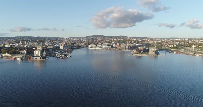 Cinema 4K drone shot with backward tilt motion revealing the forest on hoved&oslash;ya island with a background view of Bj&oslash;rvika, with the Lambda Munch Museum and Oslo Opera House in autumn, in Oslo Norway.