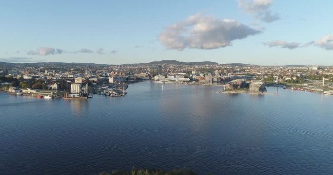 Cinema 4K drone shot with backward tilt motion revealing the forest on hoved&oslash;ya island with a background view of Bj&oslash;rvika, with the Lambda Munch Museum and Oslo Opera House in autumn, in Oslo Norway.