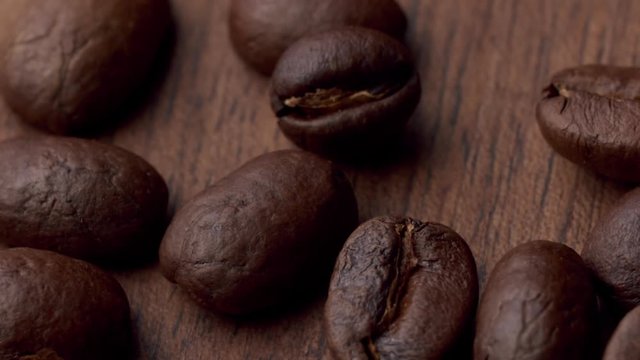 Roasted coffee beans fall on a wooden surface. Static macro top shot with commercial soft light from the side.