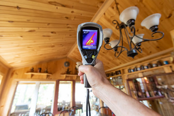 Indoor damp & air quality (IAQ) testing. A point of view perspective of an indoor environmental quality assessor at work, using a spot thermovision device to examine a wood cladding ceiling. © Valmedia
