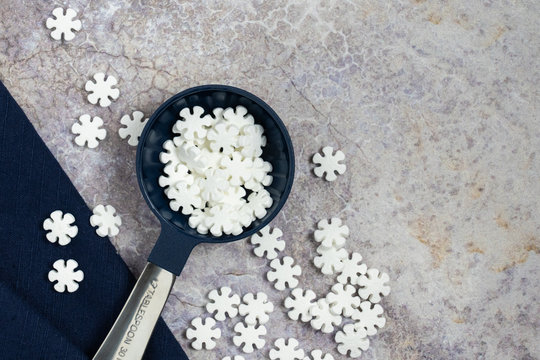 large metal and dark blue tablespoon filled with white snowflake design edible cookie decorations on a marble texture countertop background for holiday or winter baking concept