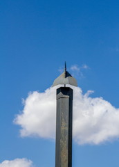Obraz premium Black metal chimney with weather vane isolated against a blue sky with a white cloud image with copy space in vertical format