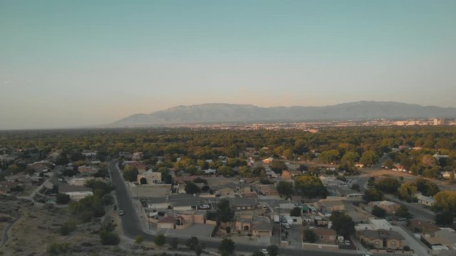 Drone flying towards the Rio Grande River’s tree line towards the city of Albuquerque, New Mexico. View of the city, and the Sandia Mountains in the background.