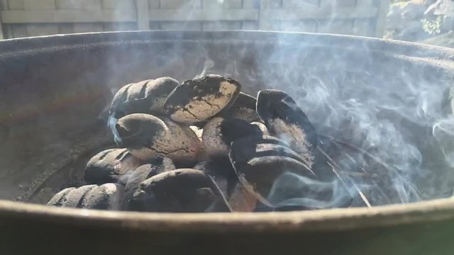 Slow motion shot of coals smoking in a kettle barbeque.