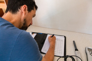 Indoor damp & air quality (IAQ) testing. A close up and rear view of a caucasian gut with short black hair, writing a report during an in-depth home inspection, with digital meters and copy space. © Valmedia