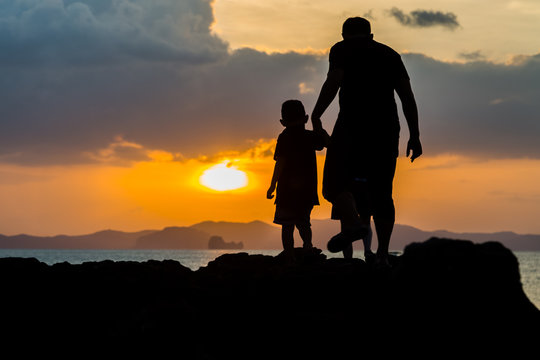 Silhouette image of father and son at the beach before sunset