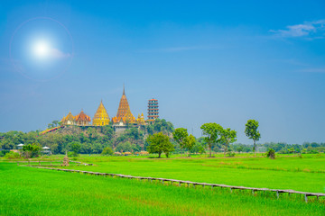 Scenery view  at Wat tham sua or tiger cave temple with green jasmince rice field,blue sky ,sun shine and long walkway bamboo bridge. Tourist attraction in Kanjanaburi.