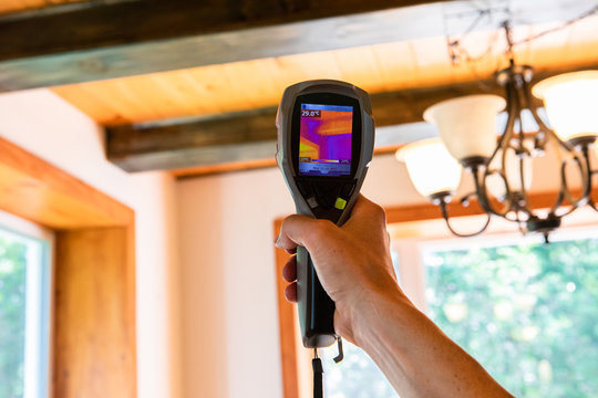 Indoor damp & air quality (IAQ) testing. A handheld IR thermovision camera is seen closeup, checking the insulation levels inside a domestic home with blurred timber beams in background.
