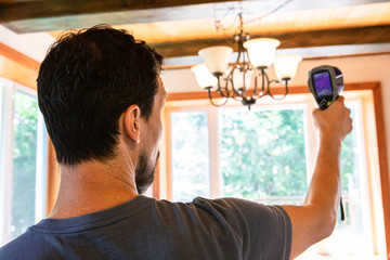 Indoor damp & air quality (IAQ) testing. A close-up and rear view of a man using thermography equipment to carry out an assessment of a residential property, checking for cold and heat sources. © Valmedia