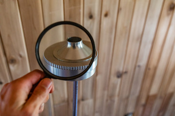 Indoor damp & air quality (IAQ) testing. A close up view of a person holding a magnifying glass by an impactor device, equipment used during indoor environmental quality assessment.