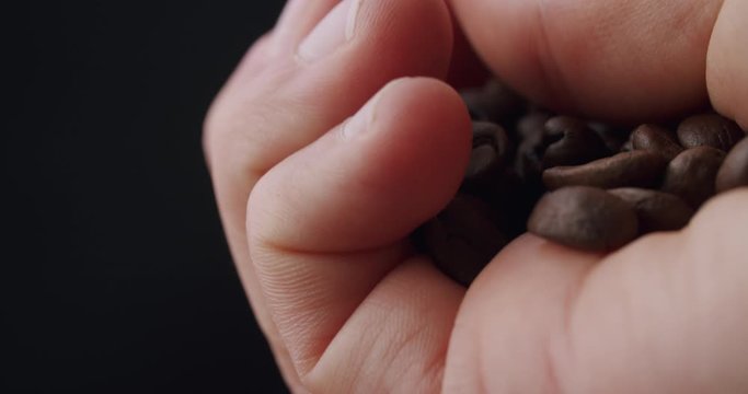 Caucasian hand holding a bunch of roasted coffee beans and inspecting the beans with thumb. Black frame at beginning and end.