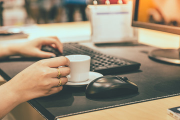 Woman hand holdding coffee cup with working table