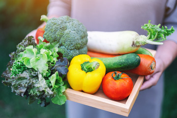 A woman holding a fresh mixed vegetables in a wooden tray