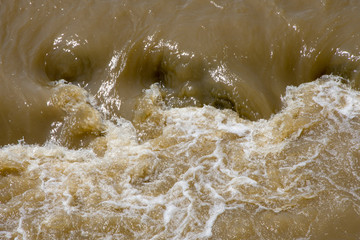 Obraz premium Brown and dirty water descends from the mountains in a seething and foaming mudflow. Floods after rains in mountainous areas.