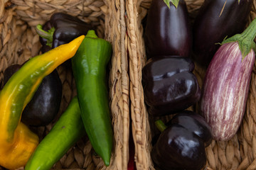 Organic produce at a farmer's market. A straight down view of long pointy peppers and eggplants in wicker baskets on a greengrocer's market stall selling biological produce.