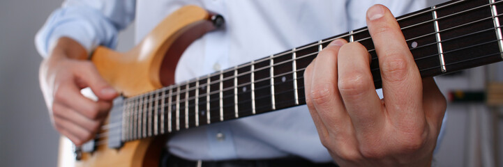 Male arms holding and playing classic shape wooden electric guitar closeup. Six stringed learning...