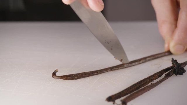 A chef delicately slices open a vanilla bean and extracts the vanilla using a very sharp knife.