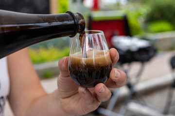 Homemade drink at farmer's market. A market trader pours a sample glass of home brewed alcoholic beverage, dark liquid pours from glass bottle, seen close up.