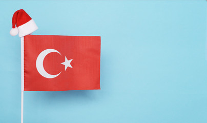 Flag of Turkey with little santa claus hat on blue background. New Year winter holiday concept, copy space