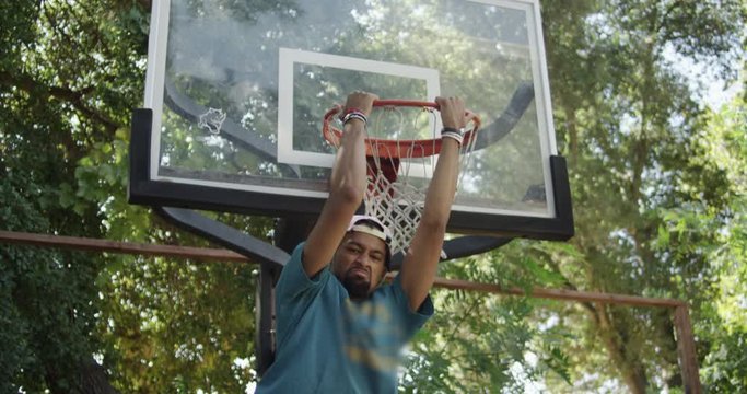 Basketball Player dunking a basketball and hanging on the rim.  Mean mugging the camera.